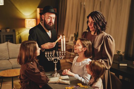 Photo for Portrait of orthodox jewish family lighting menorah candle together during Hanukkah celebration - Royalty Free Image
