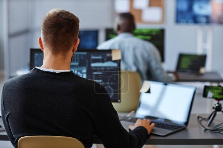 Foto de Vista posterior del programador masculino o especialista en datos utilizando la computadora en la oficina con gráficos en la pantalla, espacio de copia - Imagen libre de derechos