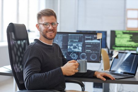 Téléchargez les photos : Portrait de programmeur logiciel souriant à la caméra tout en posant sur le lieu de travail dans le bureau avec tasse à café, espace de copie - en image libre de droit