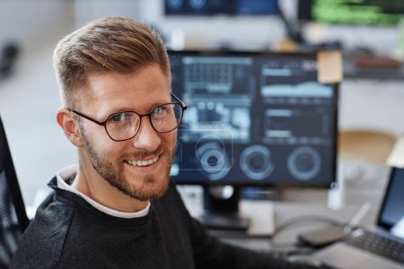 Foto de Primer plano retrato de un joven desarrollador de software sonriendo a la cámara y usando gafas en la oficina, espacio para copiar - Imagen libre de derechos