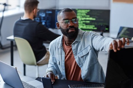 Téléchargez les photos : Portrait de l'homme noir ajustant des écrans d'ordinateur tout en écrivant le code de logiciel dans le bureau - en image libre de droit