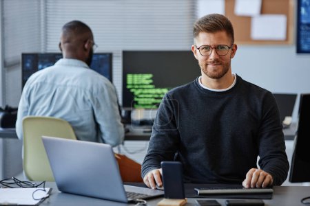 Foto de Retrato del desarrollador de software masculino sonriendo a la cámara mientras está sentado en el lugar de trabajo en la oficina, espacio de copia - Imagen libre de derechos
