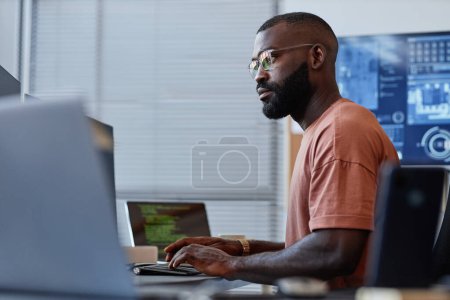 Foto de Retrato de vista lateral del desarrollador de software negro usando computadora en oficina de alta tecnología, sistemas de datos y programación - Imagen libre de derechos