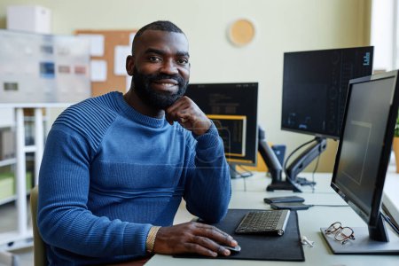 Foto de Retrato del hombre afroamericano como programador de computadoras sonriendo a la cámara mientras escribe código en el lugar de trabajo de la oficina - Imagen libre de derechos