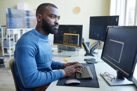 Foto de Retrato de vista lateral del hombre afroamericano como programador de computadoras escribiendo código en el lugar de trabajo de la oficina - Imagen libre de derechos