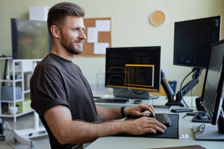 Téléchargez les photos : Vue de côté portrait de souriant homme caucasien comme programmeur informatique écriture code au bureau lieu de travail - en image libre de droit
