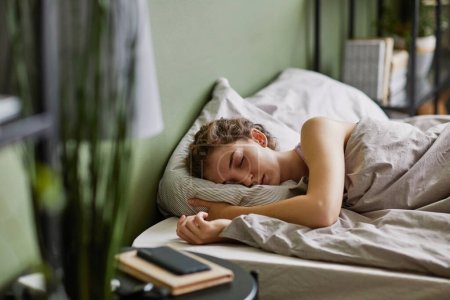 Téléchargez les photos : Jeune femme dormant sur oreiller sous couverture dans son lit dans la chambre après une dure journée - en image libre de droit
