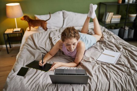 Foto de Vista de ángulo alto de la mujer joven dibujando en la tableta gráfica mientras está acostado en la cama en casa - Imagen libre de derechos