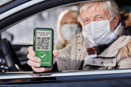 Photo for Senior man showing digital vaccination code from car window and wearing mask during winter vacation, copy space - Royalty Free Image