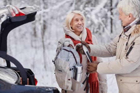 Téléchargez les photos : Portrait taille haute d'un couple de personnes âgées souriantes sortant un sac à dos de randonnée tout en profitant d'une escapade hivernale dans la nature ensemble, copiez l'espace - en image libre de droit