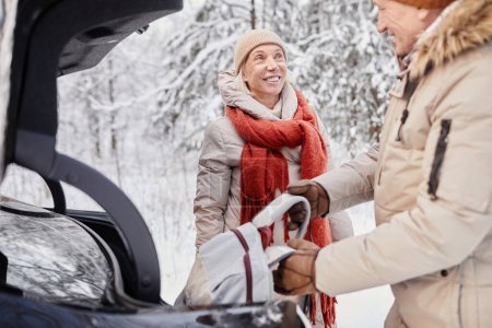 Photo for Portrait of mature couple enjoying winter getaway in nature standing by car with trunk open - Royalty Free Image
