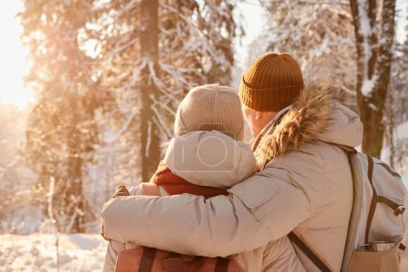 Téléchargez les photos : Vue arrière du couple d'âge mûr embrassant dans la forêt d'hiver éclairée par la lumière du soleil, espace de copie - en image libre de droit