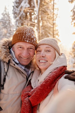 Téléchargez les photos : Point de vue vertical de heureux couple de personnes âgées prenant des photos selfie tout en profitant de la randonnée dans la forêt d'hiver - en image libre de droit