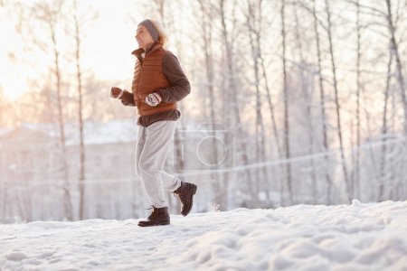 Photo for Side view portrait of sporty mature woman running in winter forest and smiling, copy space - Royalty Free Image
