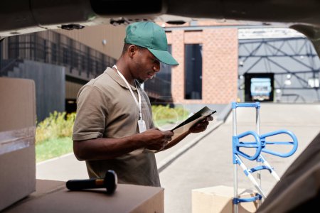 Photo for Side view portrait of young delivery man checking papers while unloading van - Royalty Free Image