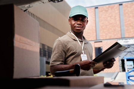 Photo for Portrait of black young man as delivery worker unloading van with packages - Royalty Free Image