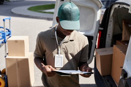 Photo for Portrait of young delivery man checking documents while unloading delivery van - Royalty Free Image