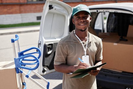 Photo for Waist up portrait of black young man unloading van with packages and smiling at camera - Royalty Free Image