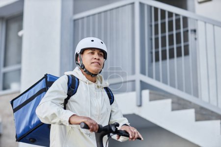 Foto de Mínimo tiro del trabajador de reparto de alimentos que lleva casco mientras monta scooter eléctrico en el entorno de la ciudad, espacio de copia - Imagen libre de derechos