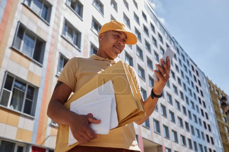 Foto de Retrato de bajo ángulo de una mujer joven entregando paquetes en la ciudad y utilizando un teléfono inteligente - Imagen libre de derechos