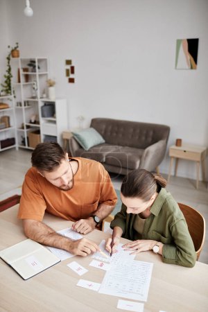 Photo for Above view of young tutor explaining new subject to student at home lesson while pointing at document with assignment or data - Royalty Free Image