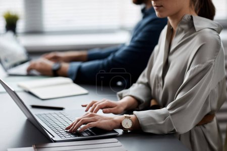 Téléchargez les photos : Jeune femme d'affaires ou étudiante en robe de soie grise tapant sur clavier d'ordinateur portable tout en recherchant des données en ligne ou en effectuant une tâche - en image libre de droit
