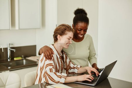 Foto de Retrato de dos mujeres jóvenes sonrientes usando un portátil juntas en casa mientras administran pequeñas empresas o estudian en línea - Imagen libre de derechos