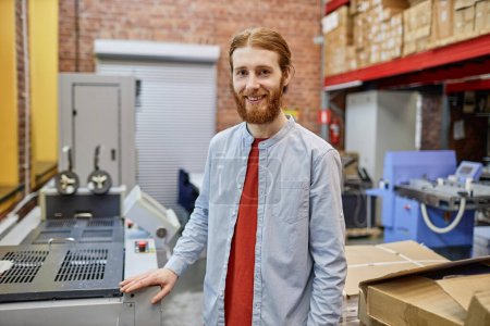 Téléchargez les photos : Portrait taille haute de jeune homme souriant travaillant dans une imprimerie industrielle et regardant la caméra, l'espace de copie - en image libre de droit