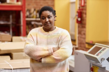Téléchargez les photos : Portrait taille haute de jeune femme noire travaillant dans une imprimerie industrielle et regardant la caméra debout les bras croisés, espace de copie - en image libre de droit