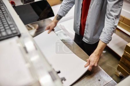 Photo for High angle view of man putting stack of paper in printing machine at publishing shop, copy space - Royalty Free Image