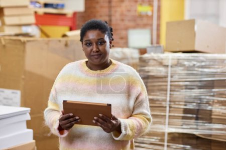Téléchargez les photos : Portrait taille haute d'une femme noire souriante tenant une tablette numérique à l'imprimerie et regardant un appareil photo - en image libre de droit