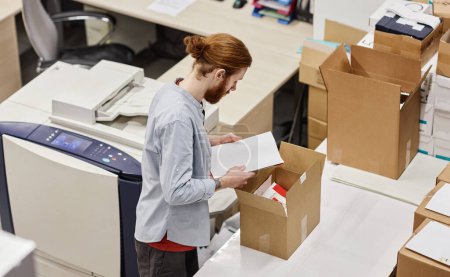 Photo for High angle portrait of young man packaging print products in publishing shop, copy space - Royalty Free Image