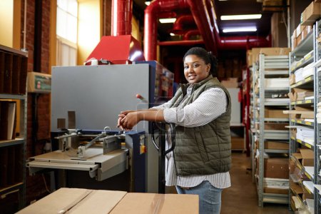 Foto de Retrato de vista lateral de la mujer negra sonriendo a la cámara mientras trabaja en la fábrica de impresión - Imagen libre de derechos