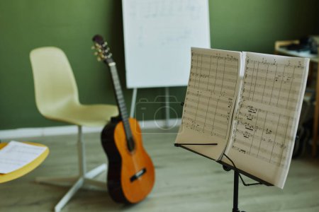 Foto de Dos papeles con notas musicales sobre soporte de música en el fondo de la guitarra, sillas para los estudiantes y pizarra para el profesor en el aula espaciosa - Imagen libre de derechos