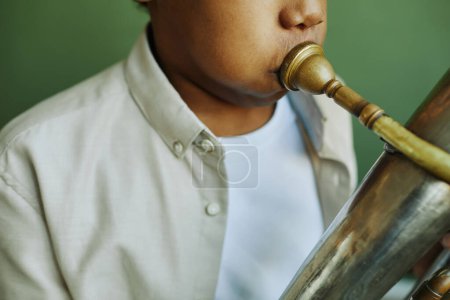 Téléchargez les photos : Gros plan d'un écolier afro-américain en tenue décontractée qui sonne de la trompette pendant un cours individuel de musique sur fond vert - en image libre de droit