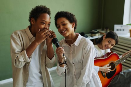Photo for Youthful schoolkids performing song together during repetition with accompaniment of acoustic guitar played by Asian schoolgirl - Royalty Free Image