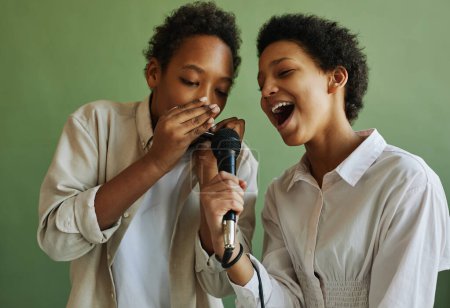 Foto de Joven chico y chica afroamericanos cantando juntos durante la repetición mientras tocan armónica y cantan en micrófono - Imagen libre de derechos