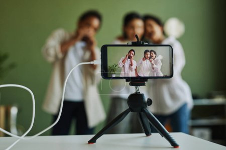Photo for Group of happy intercultural kids performing song on smartphone screen during livestream or video recording while having repetition - Royalty Free Image