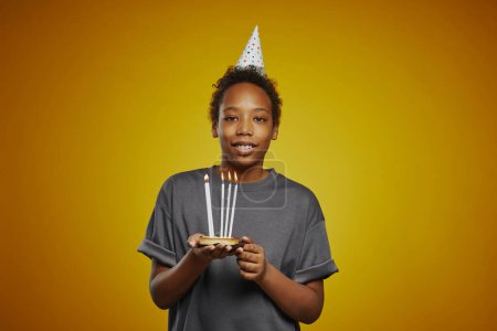 Photo for Happy youthful boy with group of burning candles standing in front of camera against yellow background and looking at you - Royalty Free Image