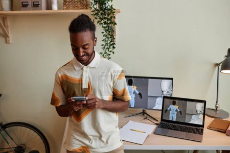 Téléchargez les photos : Portrait taille haute de l'homme noir créatif en tant que concepteur 3D numérique en utilisant smartphone par lieu de travail, espace de copie - en image libre de droit