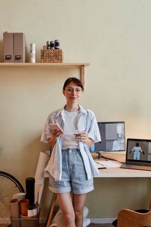 Téléchargez les photos : Portrait vertical de la jeune femme créative en tant que designer 3D numérique souriant à la caméra par le lieu de travail de bureau à domicile - en image libre de droit