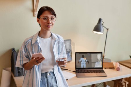 Téléchargez les photos : Portrait taille haute de jeune femme créative en tant que concepteur 3D regardant la caméra debout près du lieu de travail de bureau à la maison, espace de copie - en image libre de droit
