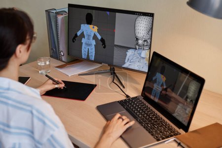 Téléchargez les photos : Jeune créatrice construisant des modèles 3D numériques pour les personnages de jeux vidéo sur le lieu de travail et en utilisant une tablette de stylo - en image libre de droit