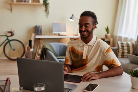Téléchargez les photos : Portrait d'un homme noir souriant utilisant une tablette de stylo au bureau à la maison pour la conception numérique ou la retouche photo - en image libre de droit