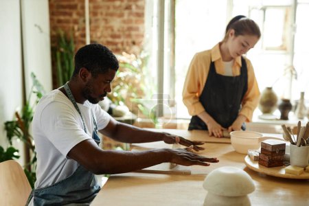 Téléchargez les photos : Portrait latéral de jeune homme noir façonnant de l'argile tout en profitant d'un cours d'art en atelier de poterie, espace de copie - en image libre de droit