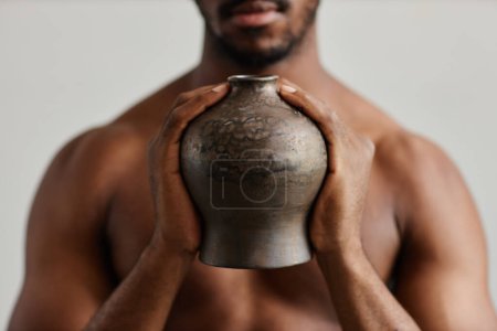 Foto de Primer plano del hombre negro sin camisa sosteniendo jarrón de cerámica bronceado con textura imperfecta, espacio de copia - Imagen libre de derechos