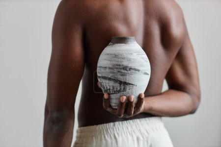 Photo for Close up of shirtless man holding handmade ceramic vase behind back complementing natural body shape, wabi sabi design - Royalty Free Image