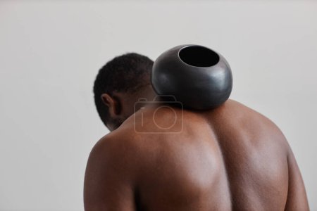 Téléchargez les photos : Homme noir torse nu tenant vase bronzé rond sur les muscles toniques du dos - en image libre de droit