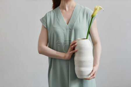 Téléchargez les photos : Gros plan minimal de la jeune femme méconnaissable tenant vase en céramique fait main avec fleur - en image libre de droit