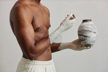 Téléchargez les photos : Minimal shot of muscular black man holding handcrafrted ceramic vase, art and artist concept - en image libre de droit